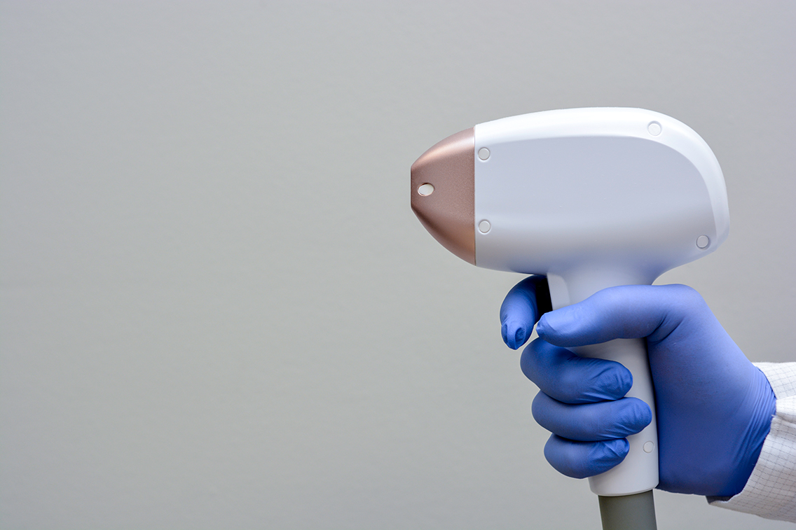 A gloved hand holds a diode laser hair removal device hand piece.